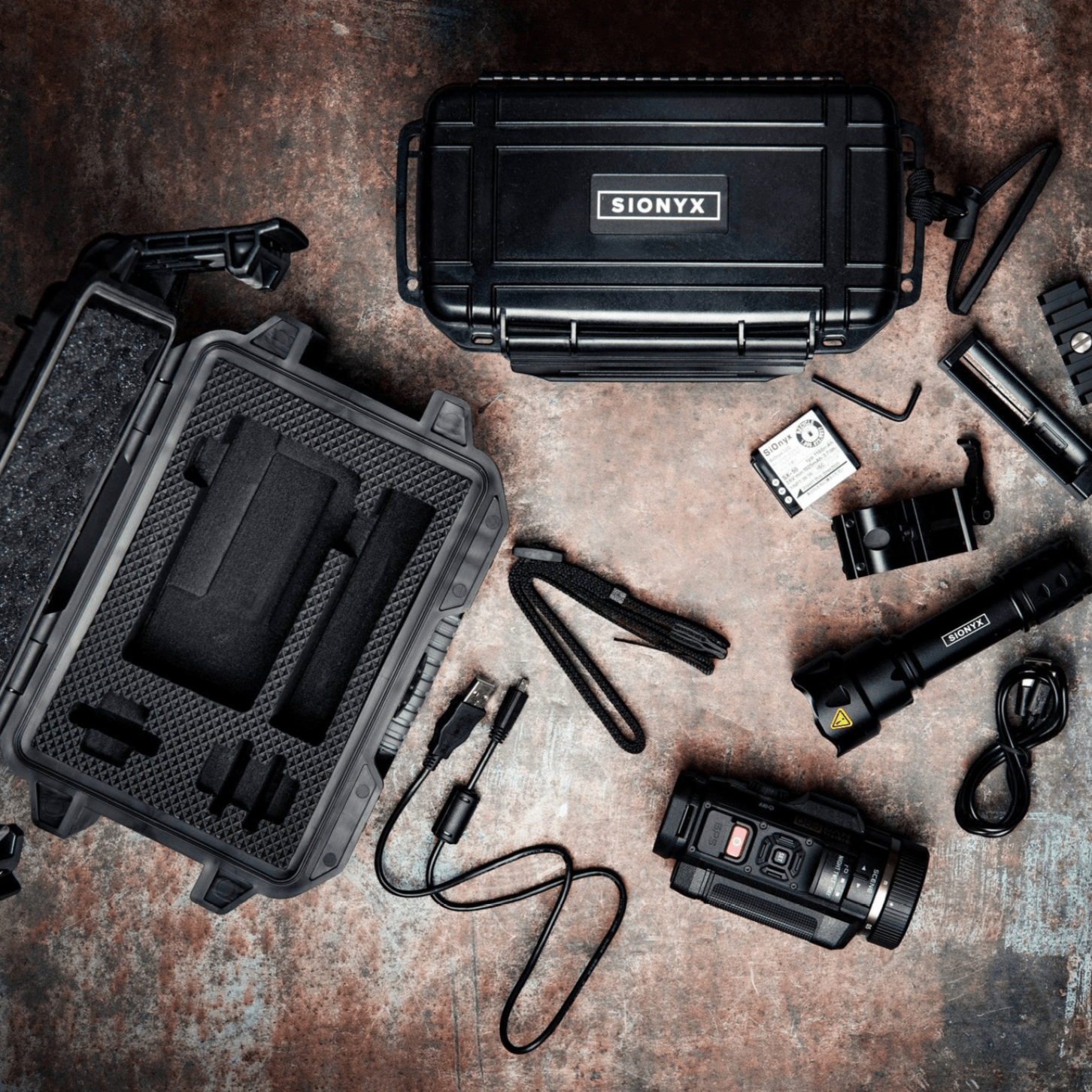 Flat lay of SiOnyx Illuminator Kit and additional gear arranged on a wooden surface, showing kit use in field-ready context