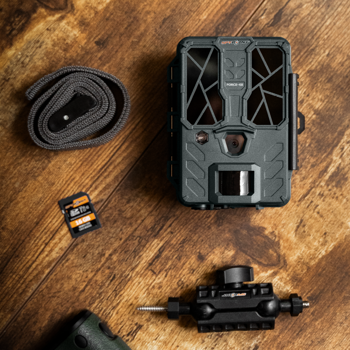 Flat lay showing SPYPOINT Force-48 camera with strap and memory card on wood surface