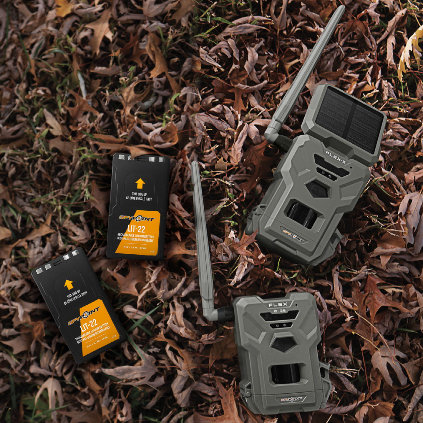 Lifestyle image showing two SPYPOINT LIT-22 batteries alongside trail cameras and packaging on forest floor